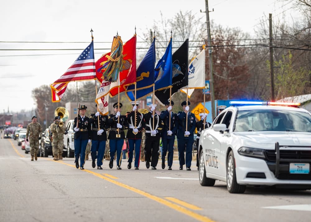 Military color guard carrying flags in the Waynesville Veterans Day Parade, with a police escort.